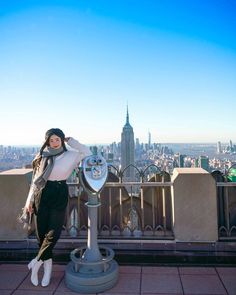 a woman standing next to a parking meter on top of a tall building in the city