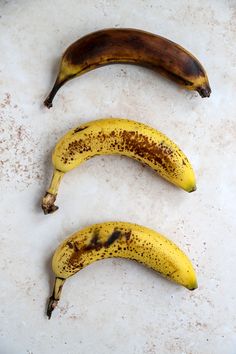 three ripe bananas sitting on top of a white counter next to each other with brown spots