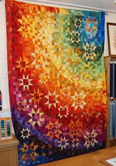 a colorful quilt hanging on the wall next to a bookshelf in a room