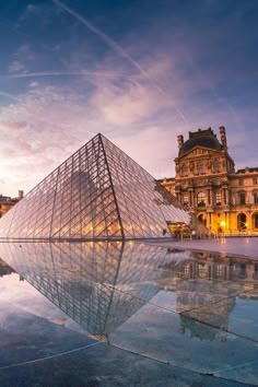 a large glass pyramid in front of a building with a reflection on the ground at dusk