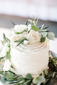 a wedding cake with white flowers and greenery on top is sitting on a plate