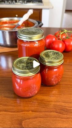 four jars filled with tomato sauce sitting on top of a wooden table next to tomatoes