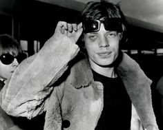 black and white photograph of man in sunglasses holding up his jacket over his head while standing next to other people