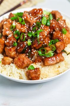 a white plate topped with rice and meat covered in sesame seeds, scallions and green onions