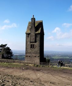 two people standing in front of a stone building on top of a hill with a fence around it