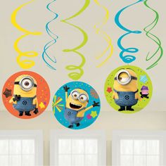 three decorations hanging from the ceiling in a room with white walls and windows, including two minion balloons