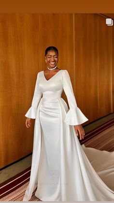 a woman in a white dress standing next to a wall with wood paneling on it