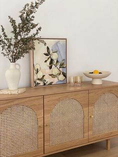 a vase with some flowers on top of a wooden cabinet next to a bowl and plate