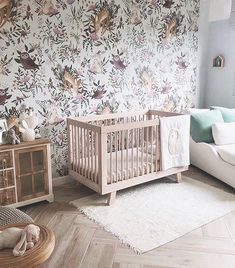 a baby crib in front of a floral wallpapered room with white furniture