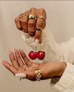 a woman holding two cherries in her hands with gold rings on each one hand