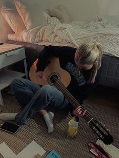 a woman is sitting on the floor with her guitar in front of her and looking down