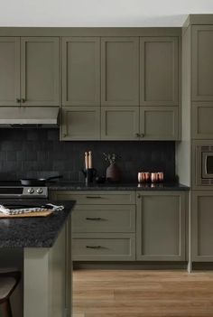 an image of a kitchen setting with green cabinets and black counter tops on the island