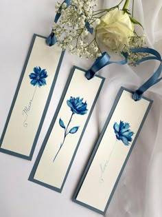 three tags with blue flowers on them next to a white rose