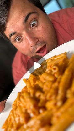 a man holding a white plate with pasta on it and looking surprised at the camera