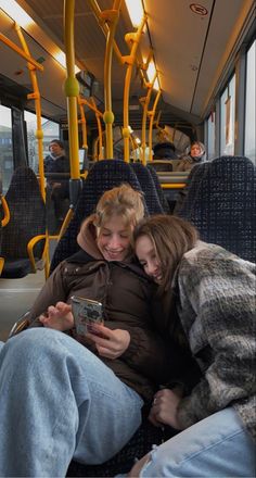 two people sitting on a bus looking at a cell phone while the man is holding his arm around the woman's shoulder