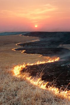 a fire hydrant on the side of a dry grass field at sunset with bright flames coming from it