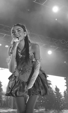 a woman standing on top of a stage holding a microphone in her hand and singing