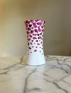 a white vase with pink and red hearts on it sitting on a marble counter top