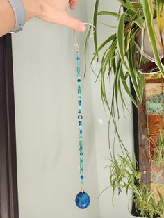 a person is holding a blue beaded necklace in front of a potted plant