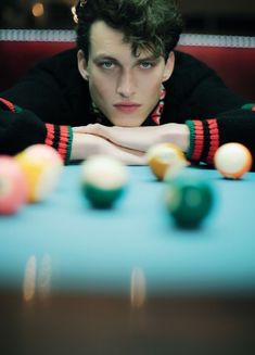 a young man sitting at a pool table with his arms crossed and balls in front of him