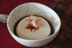 a white bowl filled with food sitting on top of a wooden table next to a spoon