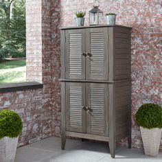 a tall wooden cabinet next to two potted plants on the side of a brick wall