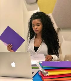 a woman sitting at a table with a laptop computer in front of her and lots of folders stacked around her