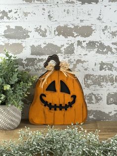 a wooden pumpkin with a jack - o'- lantern on it sitting in front of a potted plant