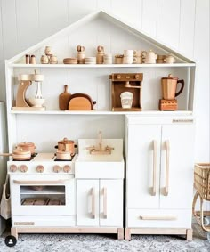 a white toy kitchen with lots of wooden toys on it's shelves and cupboards