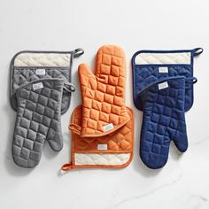 three oven mitts are lined up on a white counter top, one has an oven mitt and the other has two oven mitts