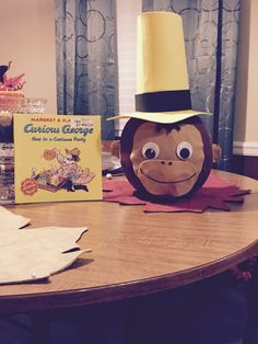 a monkey with a yellow hat on top of it's head next to a book