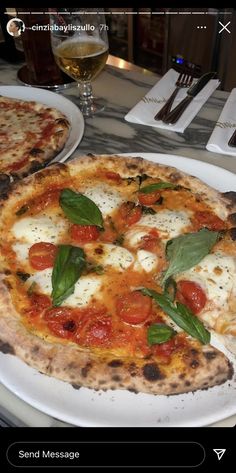 two pizzas sitting on top of a white plate next to glasses of wine and utensils