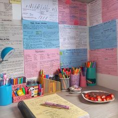 a desk with lots of papers and pencils on it, along with a plate of strawberries