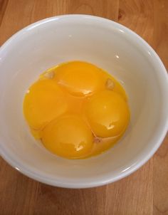 three eggs in a white bowl on a wooden table