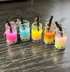 four different colored drinks in small glass jars with black straws on each one side