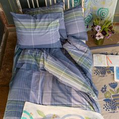 a bed with blue and green plaid comforter next to a flower pot on the floor