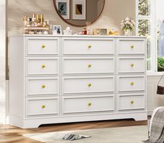 a white dresser with yellow knobs in a living room next to a mirror and window