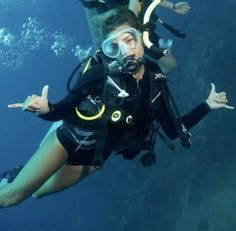 two people in scuba gear diving under the water with their hands up and pointing at something