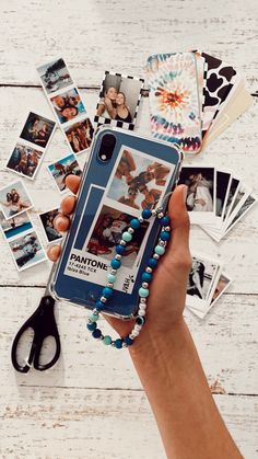 a person holding a cell phone in their hand with pictures on the table behind them