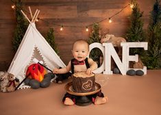 a baby sitting in front of a cake with the word one on it and a teepee tent