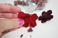 a hand holding a red felt flower next to some beads