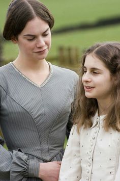 two women standing next to each other in front of a field