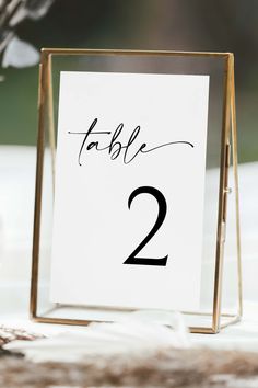 a table number is placed in a gold frame on top of a white table cloth