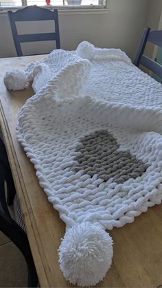 a crocheted tablecloth with pom - poms on it sitting on a wooden table