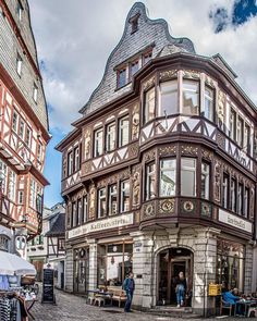 an old building with people sitting at tables in front of it on a cobblestone street