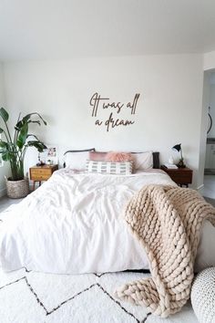 a bed with white sheets and blankets on top of it in a room filled with plants