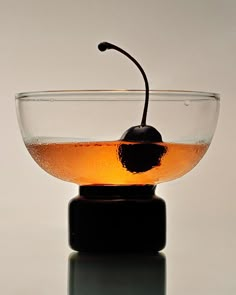 a glass bowl filled with liquid and a black cherry on the top, sitting on a reflective surface