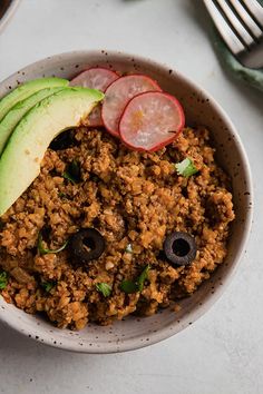 a white bowl filled with food next to an avocado and sliced radishes