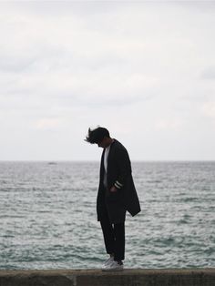 a man in a suit standing on the edge of a pier looking at the water