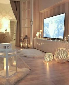 a living room filled with lots of white furniture and candles in front of a flat screen tv